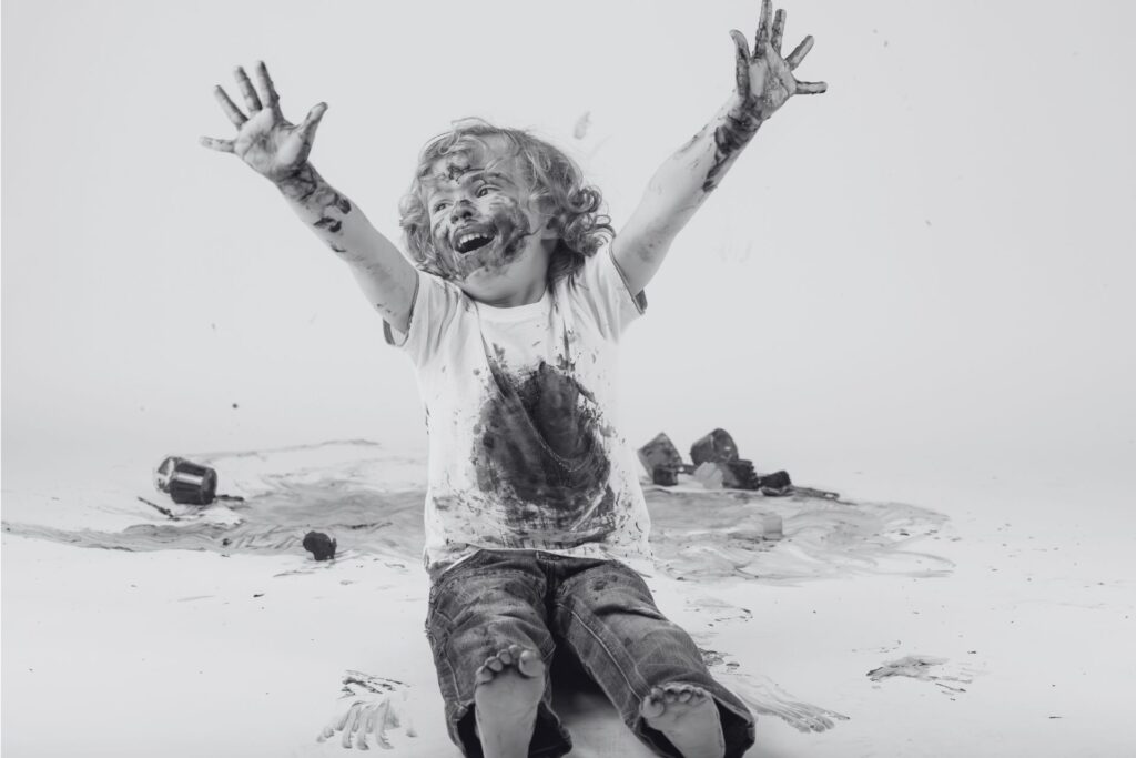 a child covered in paint raises his arms happily