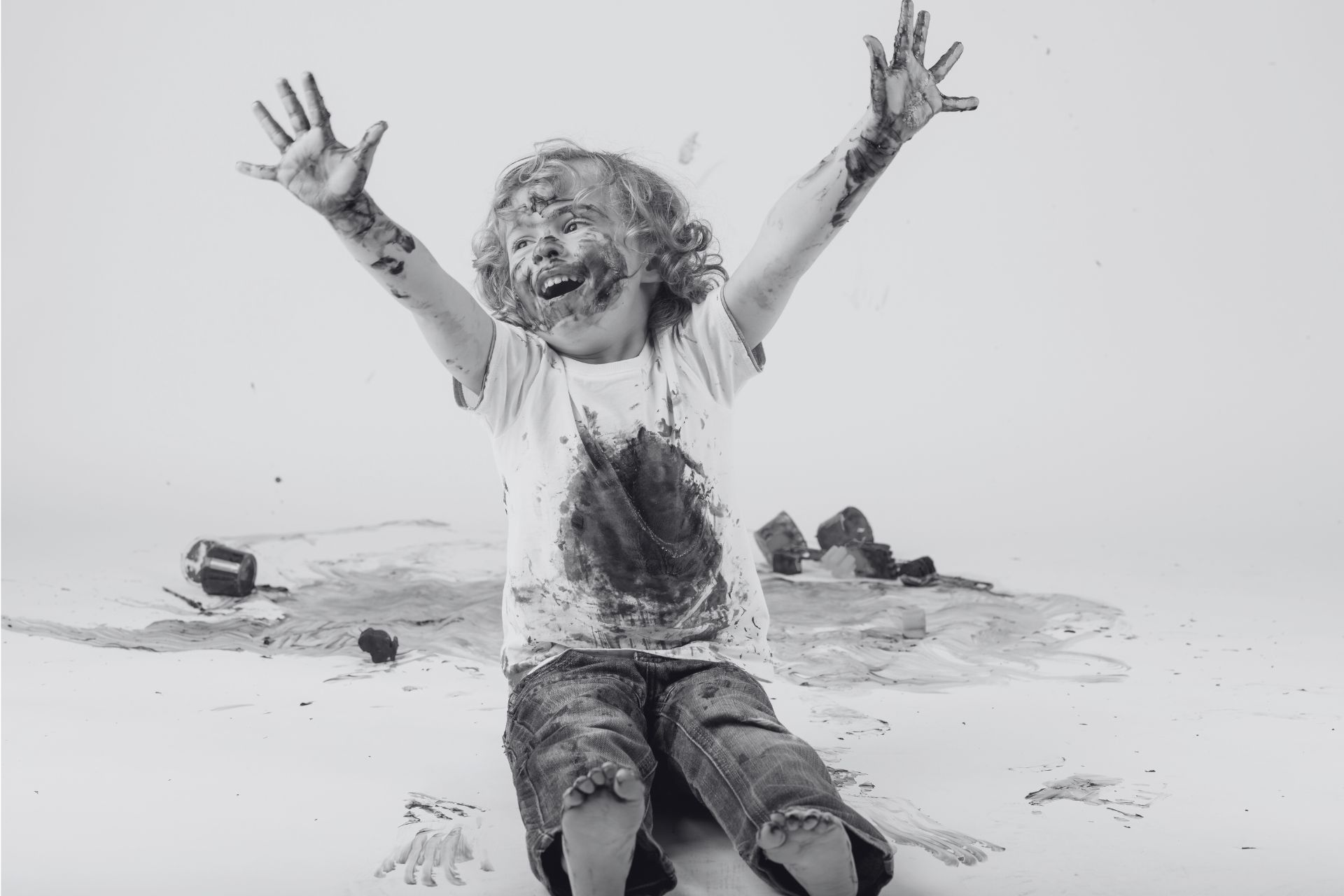 a child covered in paint raises his arms happily